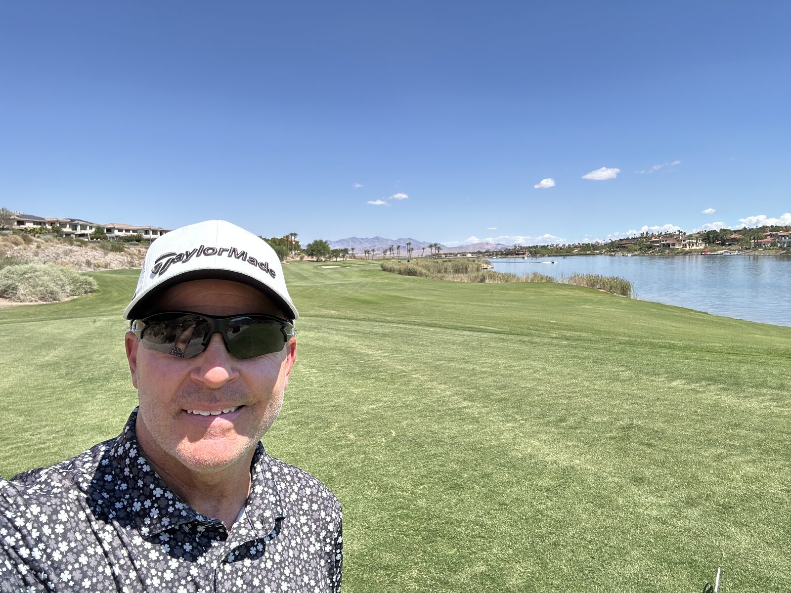 Glenn Ritter on a green fairway beside a lake, wearing a cap and sunglasses on a clear day
